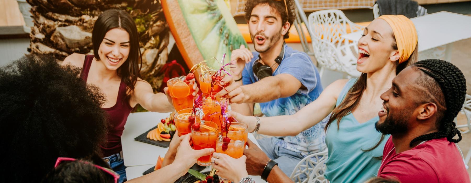 a group of people with drinks around a table of food